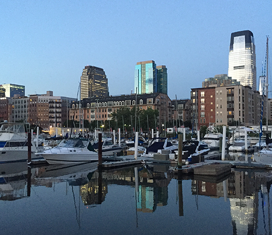 View of Hudson Pointe Marina with small boats docked in front of city buildings at dusk