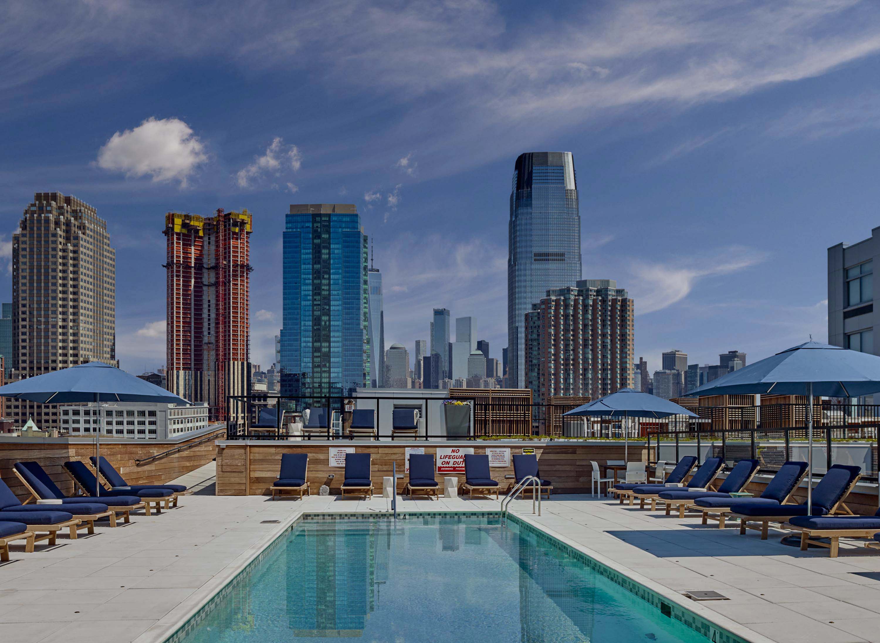 Rooftop pool deck with city views. Lounge chairs and umbrellas plus green lawn space.