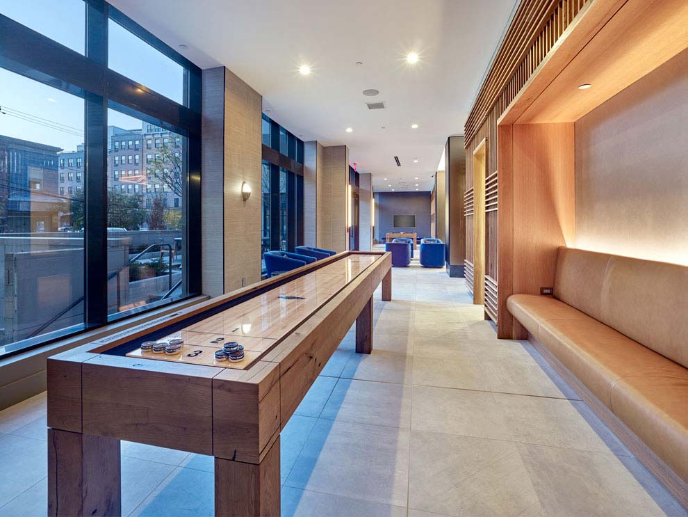 Interior of game room with shuffleboard table, leather banquet seating and views of rooftop.