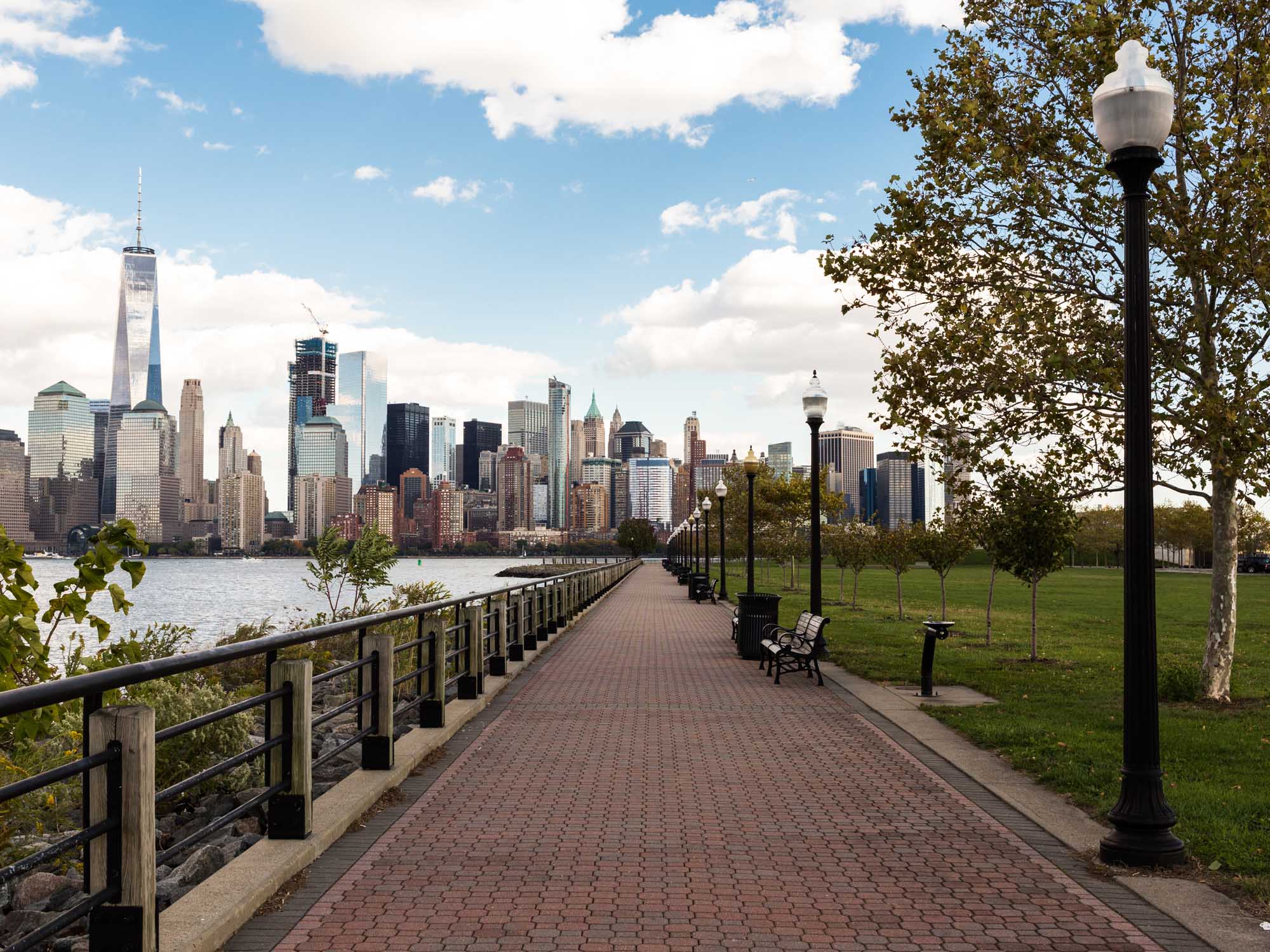 Jersey City waterfront walkway, Manhattan and Hudson River views with park to the right.