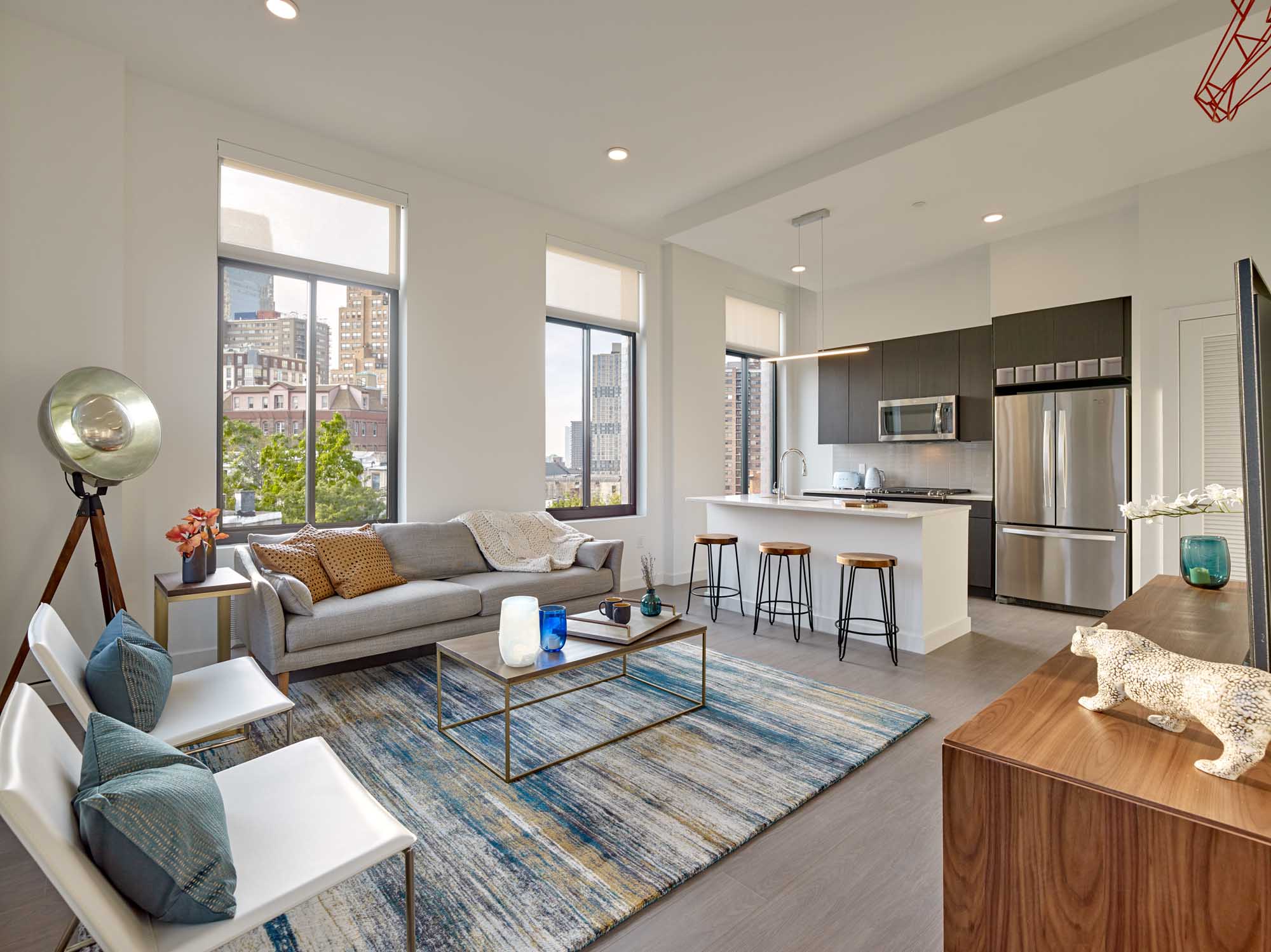 Living room with rug over hardwood floors, chair and couch with city buildings visible outside.