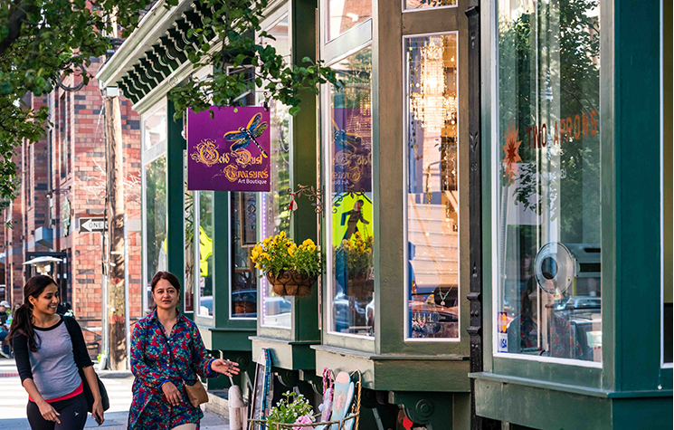 Mother and teen daughter walk street in front of art boutique store with flowering basket in window